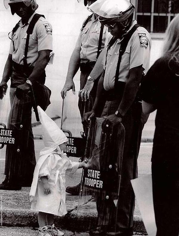 27. Bir KKK üyesinin çocuğu siyahi bir polisin kalkanında kendi yansımasına dokunuyor.