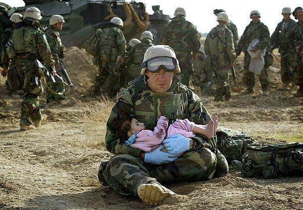 8. ABD Deniz Kuvvetleri Hastanesi'nden bir asker açılan ateşte ailesinden ayrı düşen kız çocuğunu kucağında sakinleştirmeye çalışıyor. (Irak savaşı, 2003)