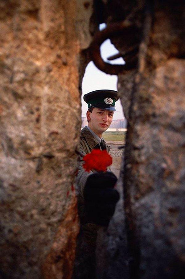 8- Berlin Duvarındaki bir çatlaktan çiçek uzatan Batı Almanya askeri (1989).