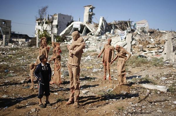 28. İsrail ile Hamas arasında yapılan son çatışmalar sonrası evlerini terk eden Filistinlileri tasvir eden Filistinli sanatçı Eyad Sabbah tarafından kil kaplı fiberglass ile yapılmış heykellere bakan Filistinli çocuk. Gazze, Filistin. 21 Ekim