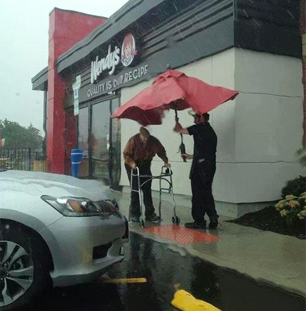 16. Bir restoran çalışanı, masadan çıkardığı şemsiyeyle yaşlı adamı yağmurdan koruyor.