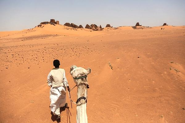 2. Meroe piramitlerini keşfe çıkan turistleri beklerken devesiyle dolaşan rehber