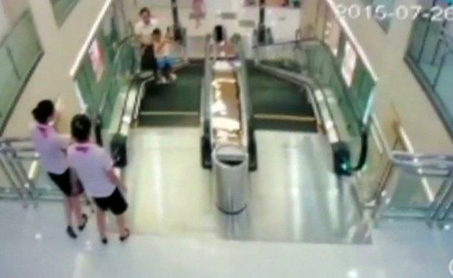 Resimdeki beyaz tişörtlü ve siyah etekli kadın, 30 yaşında bir anne ve yürüyen merdivenin sonuna yaklaşırken oğlunu kucağına alıyor. Merdiven başında bekleyen diğer iki kişi ise avm görevlileri.
