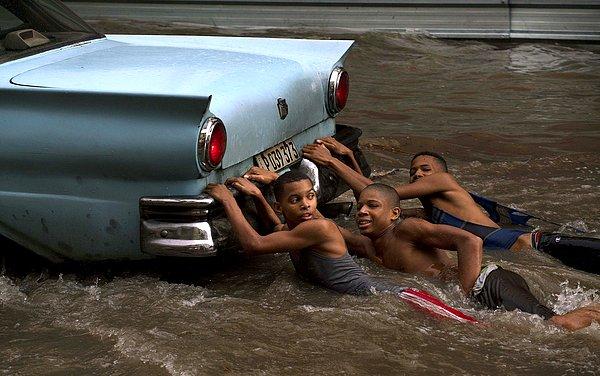 5. Havana, Küba'da çocuklar şiddetli yağmurun ardından bir arabanın arkasına tutunmuş giderken.