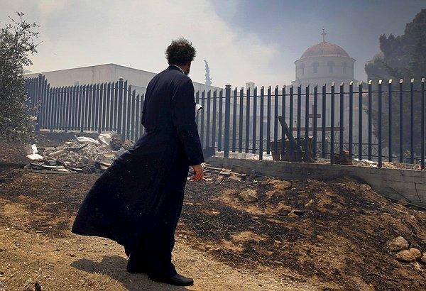 14. Yunan bir Ortodoks rahip, arkada görülen Saint George Kilisesi'nin yakınında çıkan bir yangının ardından. (17 Temmuz)