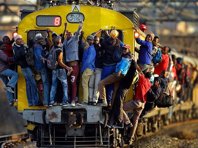 11. Güney Afrika'nın Soweto şehrinde, fazlasıyla dolu olan bir trenin önüne, arkasına ve kenarlarına tutunmuş yolcuları görüyoruz.
