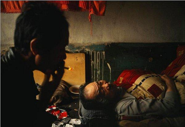 9. Çin'de, uyuyan yatalak babasının başında çaresizce sigara içen genç adam
