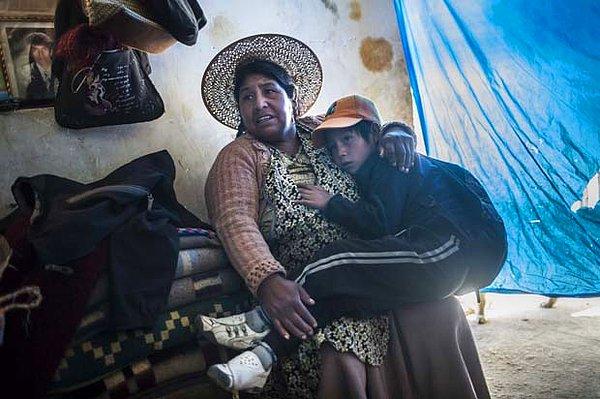 Maxima Limachi, en küçük çocuğu Israel’i kollarında tutarken. Pencere pervazında vefat etmiş eşinin fotoğrafı var. Eşi, 35 yaşındayken Cerro Rico’nun maden tünellerinin birinde geçirdiği bir kaza nedeniyle vefat etmiş. O zamandan beri, Maxima çocuklarını tek başına büyütmeye çalışıyor.