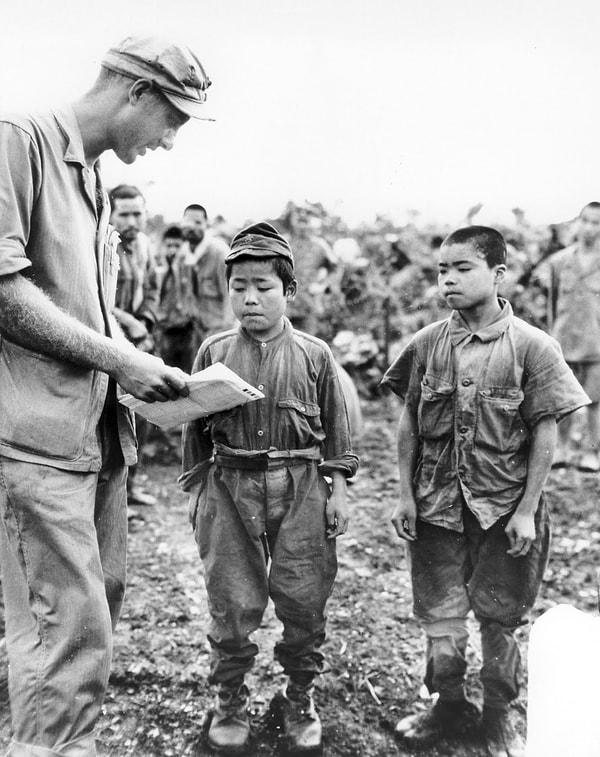 13. Okinawa'da esir düşen iki Japon askeri ile işaret dili kullanarak iletişim kurmaya çalışan bir asker. Soldakinin "18"  sağdakinin ise "20" yaşında olduğu belirtiliyor, 17 Haziran 1945.