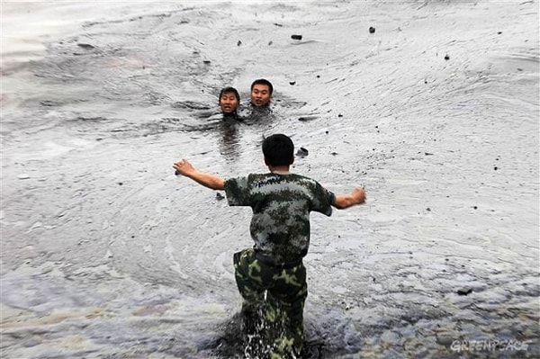25. Рабочие пытаются выбраться из воды во время ее очистки от огромного нефтяного пятна, город Далянь