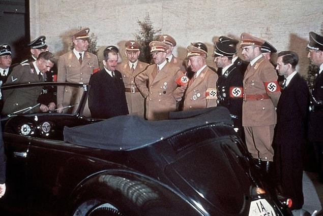 19. Automobile engineer Ferdinand Porsche (in suit) and Adolf Hitler admire Hitler's birthday gift on his 50th birthday: a convertible Volkswagen, 1939