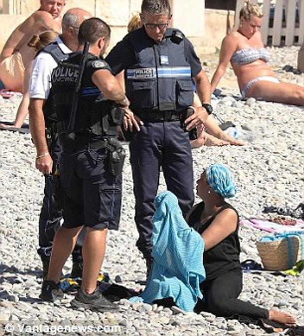Polislerin konuşmasından sonra çevredekilerin bakışları arasında kadın kıyafetini çıkarmak zorunda kalıyor.