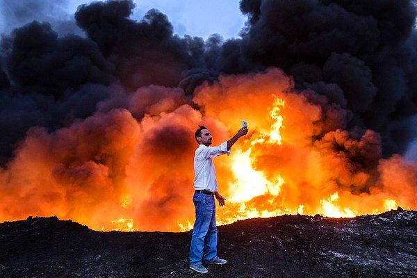 5. Musul'da süren çatışmalarda şehrin güneyindeki bir bölgede yakılan petrol ile selfie çeken adam.