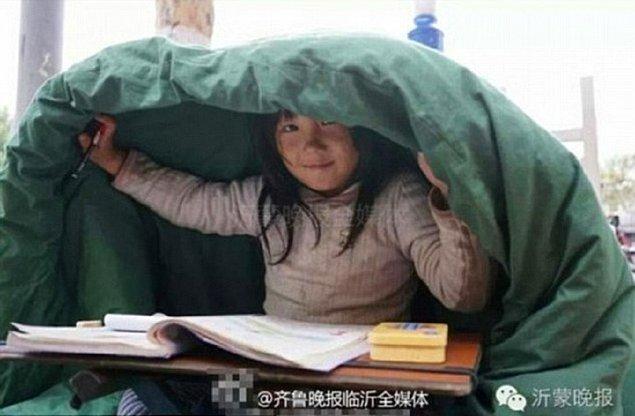 6 yaşındaki Ji soğuk rüzgardan korunabilmek için bu örtünün altına giriyor ve ödev yapıyor.