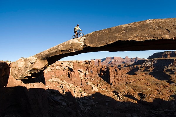 9. Горный велосипедист пересекает мост из песчаника в Национальном парке Каньонлендс, штат Юта, США