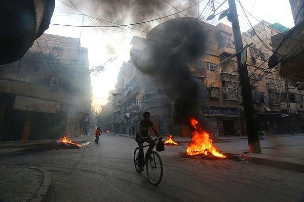 17. Muhalif güçlerin hava saldırılarına karşı dumandan bir perde oluşturmak için araba lastiklerini ateşe verdiği sokaktan geçen bir bisikletli.