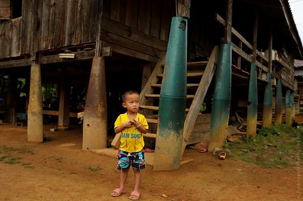26. Мальчик стоит возле своего дома, сваи которого сделаны из корпусов бомб, сброшенных самолетами ВВС США во время войны во Вьетнаме. Бан Напиа, Лаос, 3 сентября 2016 года