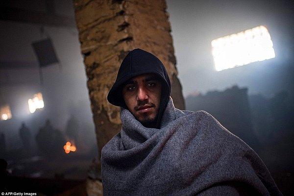 Terk edilmiş depoda battaniyesine sarınmış bir Afgan göçmen.