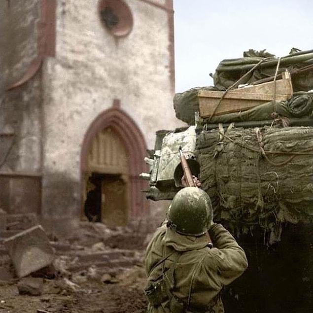 13. An American soldier from Company B, 68th Armored Infantry Battalion, 4th Armored Division, engages German snipers entrenched in a spire of the church of Saint-Michel. Alsace, France. February 6 1945.