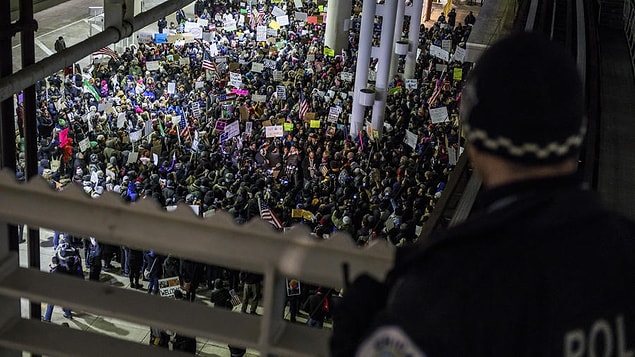 Protestocular O'Hare Uluslararası Havalimanı 5 No'lu terminal önünde bir polis memurunun bakışları önünde toplanmış halde.