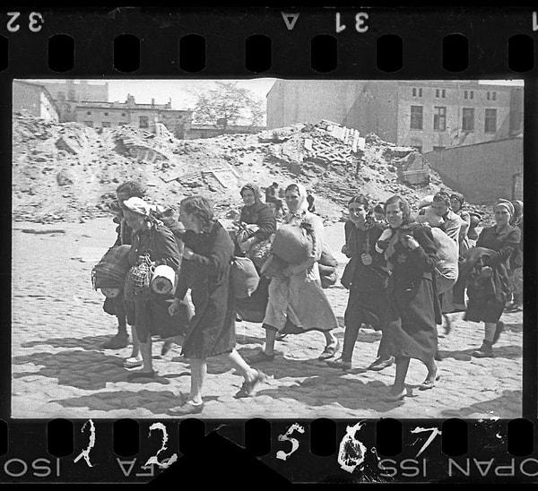 1940-1944 Bir grup kadın çuvallar ve kovalarla sinagogun yanından sürgüne doğru yürüyor.