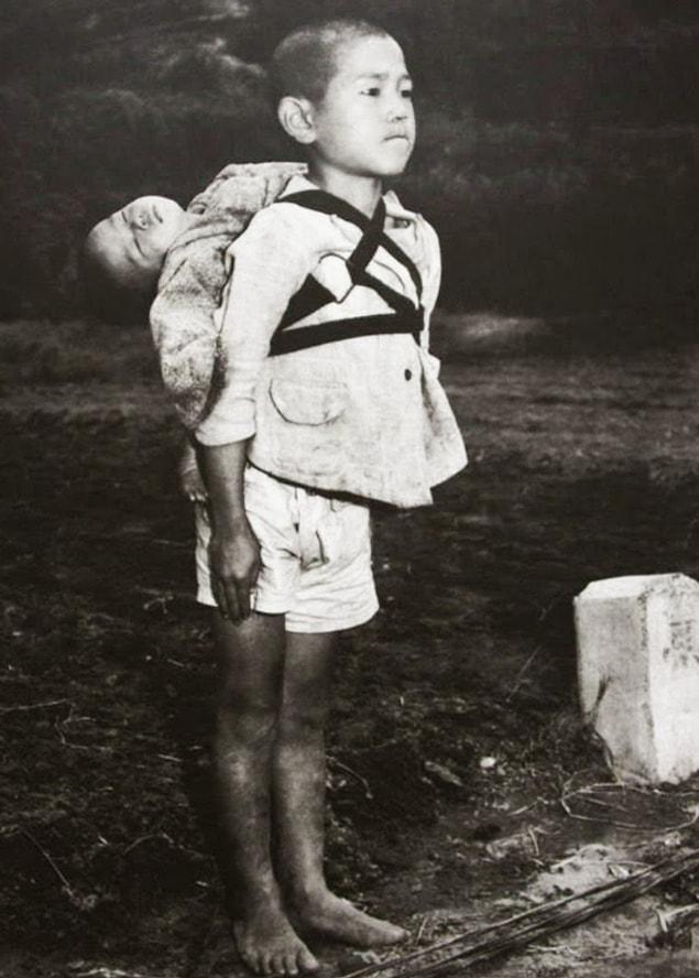 11. After the US bombings in 1945, the Japanese kid carrying what is probably his brother's dead body on his back.