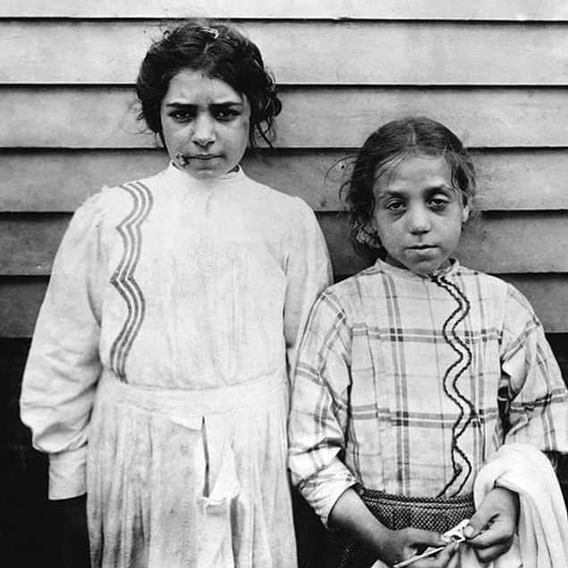17. Left: An 11-year-old newspaper carrier smiles for a portrait in New Jersey in 1924. Right: A pair of exhausted girls stand for a portrait on a break from their jobs as garment workers in the Somerville, New Jersey, tenement district in 1912.