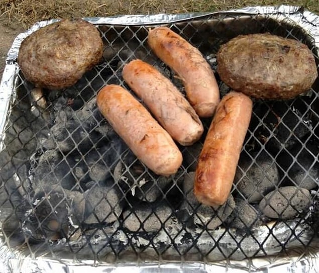 15. Slightly burned sausages and burgers, prepared on a disposable barbecue.