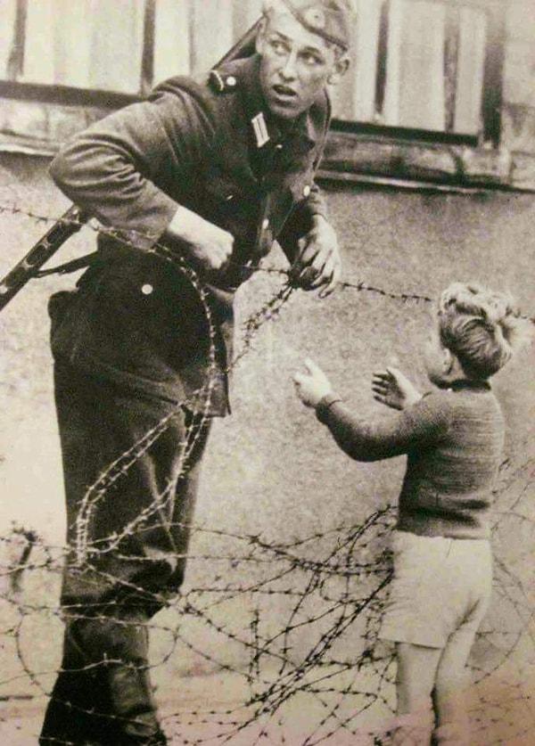 25. Doğrudan emirlere karşı gelerek, yeni kurulan Berlin Duvarı sebebiyle ailesinden ayrı düşmüş küçük çocuğun çitlerden geçmesine yardım eden Alman askeri, 1961.