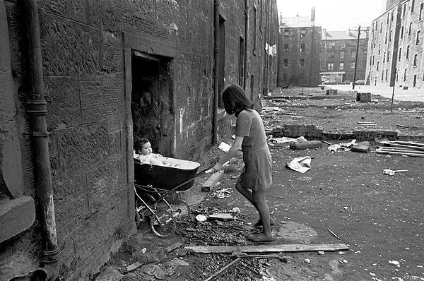 14. Fakir ailelerin elektrik ve su olmadan yaşamaya çalıştığı bir bölge olan Gorbals enkazında bebek arabasını evine süren genç bir anne, Glasgow, İskoçya, 1970.