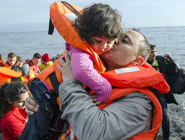 15. Беженец успокаивает маленькую девочку поцелуем по приезде на остров Лесбос в Греции (2016 год)