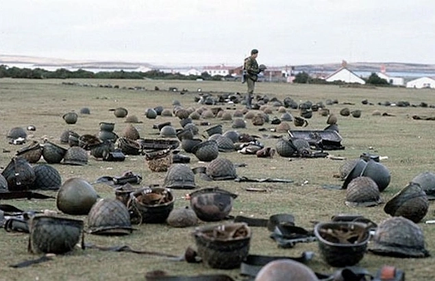 Falkland Adaları'ndaki muharebelerin birinin ardından, Arjantinli askerlerin kasklarını kontrol eden İngiliz askeri, 1982.