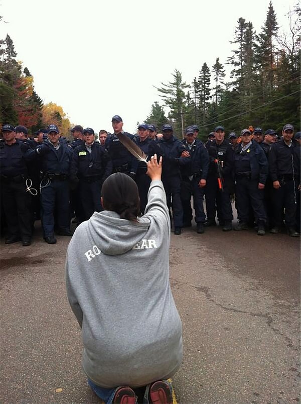 18. Kanada, New Brunswick'teki protestoda, diz çöküp polislere kuş tüyü uzatan kadın