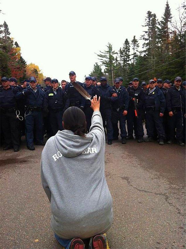 18. Kanada, New Brunswick'teki protestoda, diz çöküp polislere kuş tüyü uzatan kadın