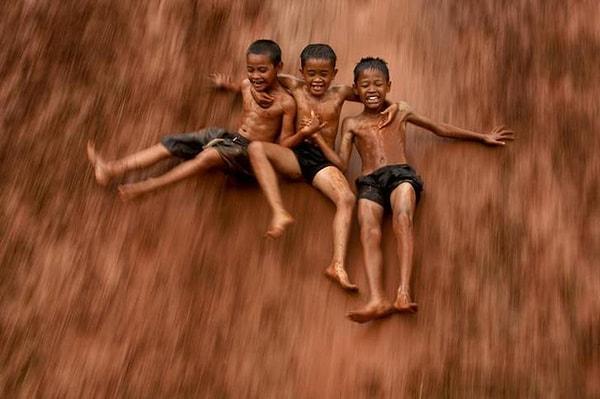 12. Jakarta'daki çamurlu tepelerden kayan üç çocuk.
