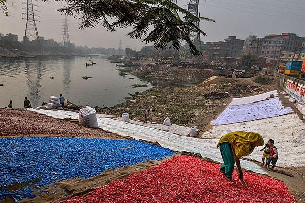 "Toplanıp yıkanan ve elle ayrılan renkli plastik parçaları Buriganga kıyılarında kuruyor. Günde 11,000 ton atık çıkaran 18 milyon nüfuslu Dakka'nın içinde ve çevresinde, serbest geri dönüşüm endüstrisinde yaklaşık 12,000 kişi çalışıyor."