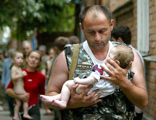 87. Beslan kasabasında ağır silahlı, maskeli erkek ve kadınların esir aldığı bir okuldan serbest bırakılan bebeği taşıyan bir Rus polis memuru - 2004