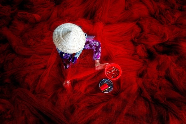 14. На этом фото запечатлена вьетнамская женщина в конической шляпе, вручную традиционным способом изготавливающая красные сети