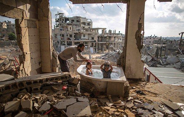 Bir baba, bombalanmış bir evin banyosunda çocuklarını yıkıyor, Gazze.