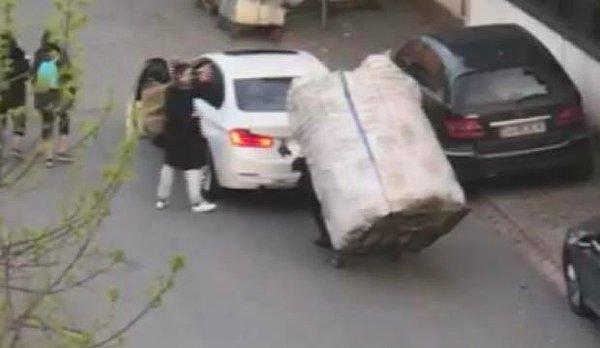 Kadın, atık kağıt yüklü el arabasını otomobiliyle çekerek yokuştan çıkardı.