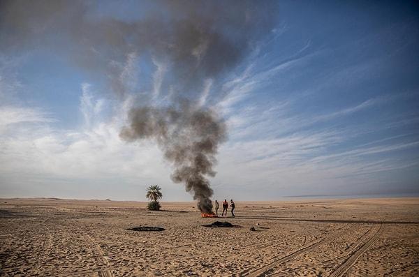 16. Libya'ya dönerken Agadez, Nijer'in ötesindeki çölde kamyonları bozulan bu göçmenler ısınmak için tekerlek yakıyor. Pascal Maitre imzalı bir fotoğraf.
