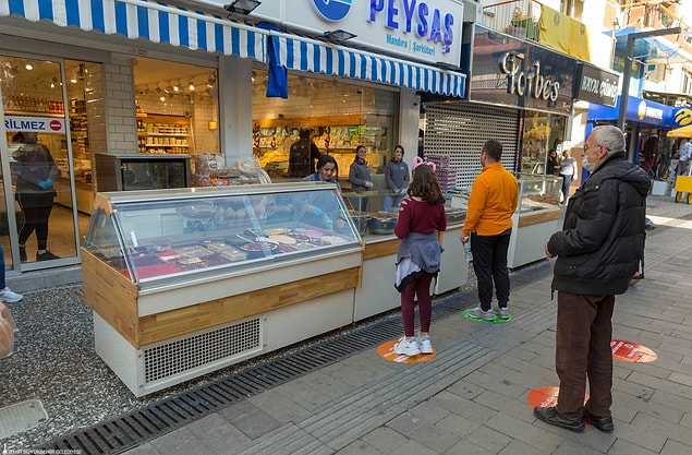 Zemin çıkartmalarının üzerinde “Sağlığın için mesafeni koru. 1 metre yeterli” gibi uyarılar yer alıyor.