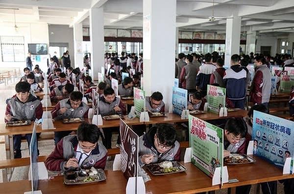 11. Çin'de başka bir okulda öğrenciler öğle yemeklerini tek başlarına yiyorlar. Koronavirüsün yayılmasını engellemek amacıyla seperatörler bulunuyor masalarda.