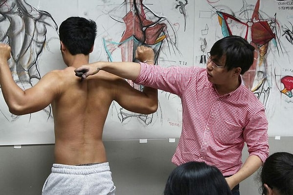 Ваннарит учит своих учеников рисовать с реального человеческого тела, указывая на мышцы, которые нужно изобразить на бумаге.