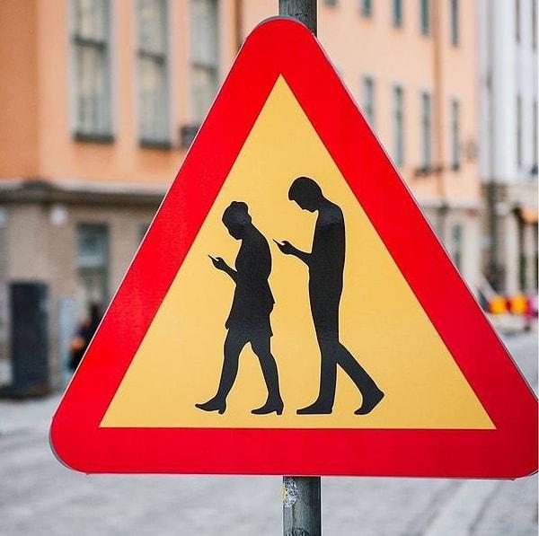 2. Araba kullanıcılarını telefonlarına bakan yayalar hakkında uyaran bir trafik işareti.