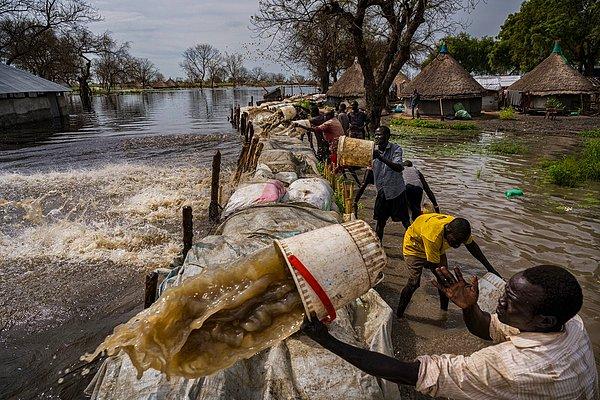 3. Lynsey Addario'nun karelediği bu görselde Güney Sudan'ın Jonglei eyaletinde barajın aşılmasına neden olan yağmurun ardından erkekler Paliau köyünden su çıkarmaya çalışıyor.