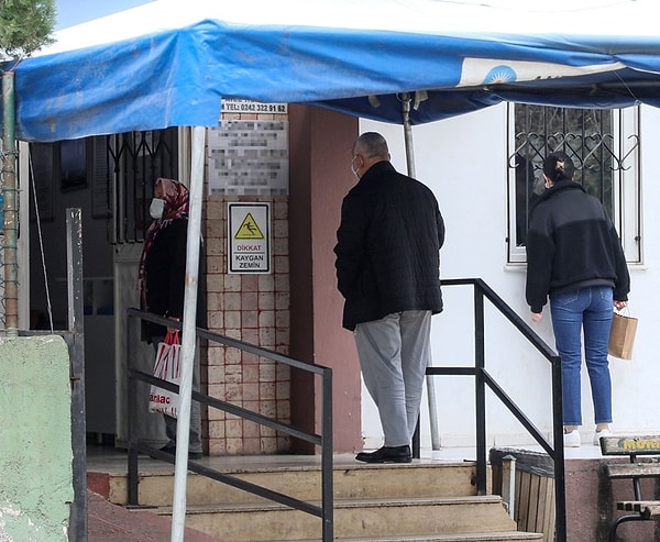 Hastanın diğer sağlık merkezlerinde içeri alındığını söylemesi üzerine doktor, "Bizim havalandırmamız yeterli değil" yanıtını verirken, kapı önündeki kişiye ne şikayeti olduğunu soruyor ve telefonunun ışığıyla bademciğine bakıyor...