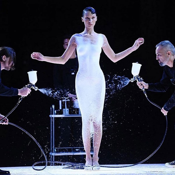 25-летняя супермодель привлекла внимание, когда появилась почти обнаженной, стоя на освещенном пьедестале, где двое мужчин начали распылять на ее кожу жидкую ткань.