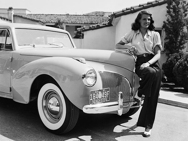 9. Rita Hayworth, yüksek belli pantolon ve katlanmış bir gömlekle bir otomobilin yanında poz veriyor.