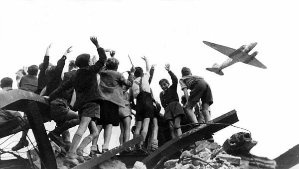 13. 1948'te, Sovyetler Birliği'nin yemek ambargosundan sonra Batı Berlin'e yiyecek taşıyan Amerika uçaklarını izleyen Berlinli çocuklar👇